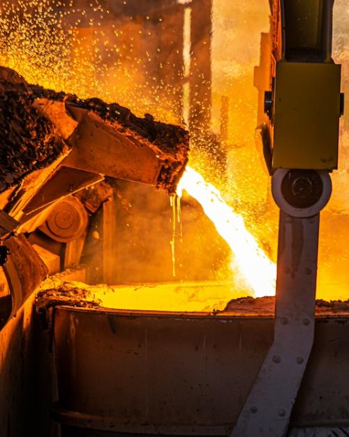 Yellow hot molten steel pours out of a shute into a vat
