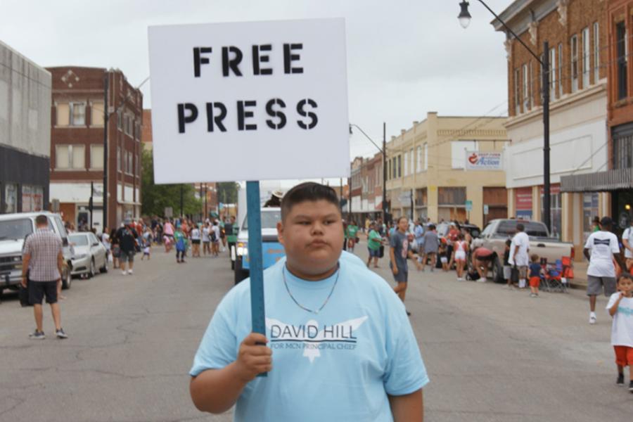 Person wearing a blue t-shirt and carrying a sign stenciled with "Free Press"